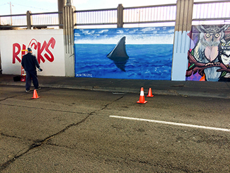 Photo of a local urban artist painting a mural under the I-70 viaduct during the 'duct-work Event.