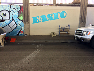 Photo of a local urban artist painting a mural under the I-70 viaduct during the 'duct-work Event.